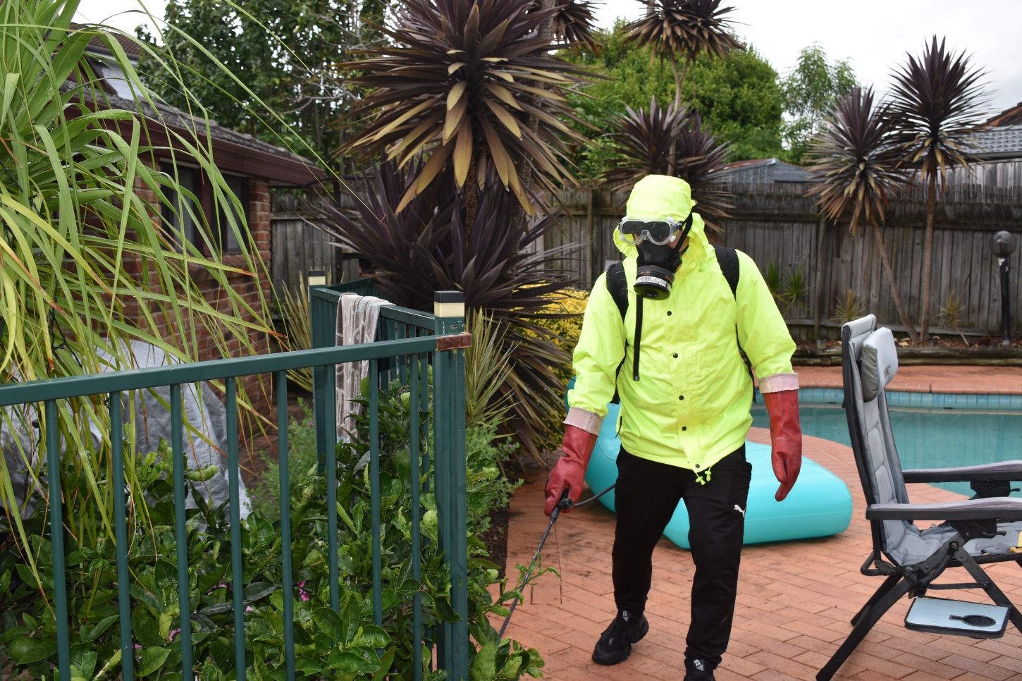 A Kill and Chill Pest Experts technician in protective gear spraying pest treatment around a backyard pool in Hornsby