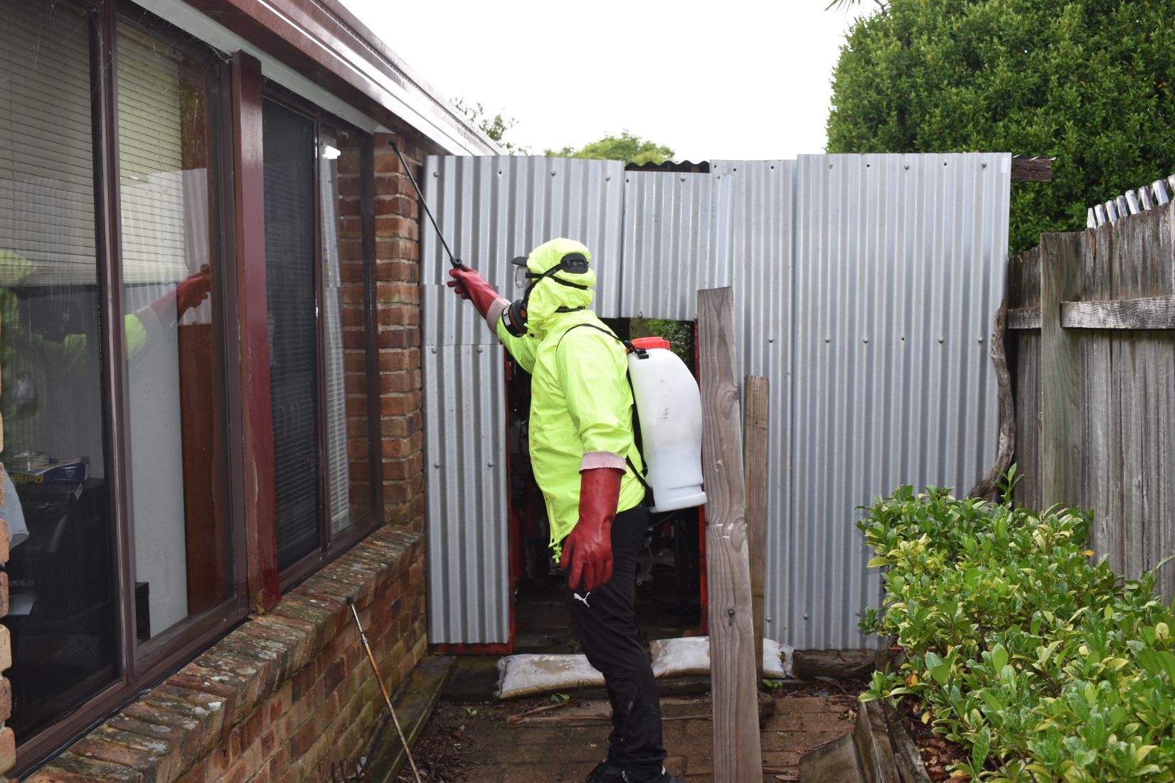 A Kill and Chill technician with a backpack sprayer treating the eaves of a brick home